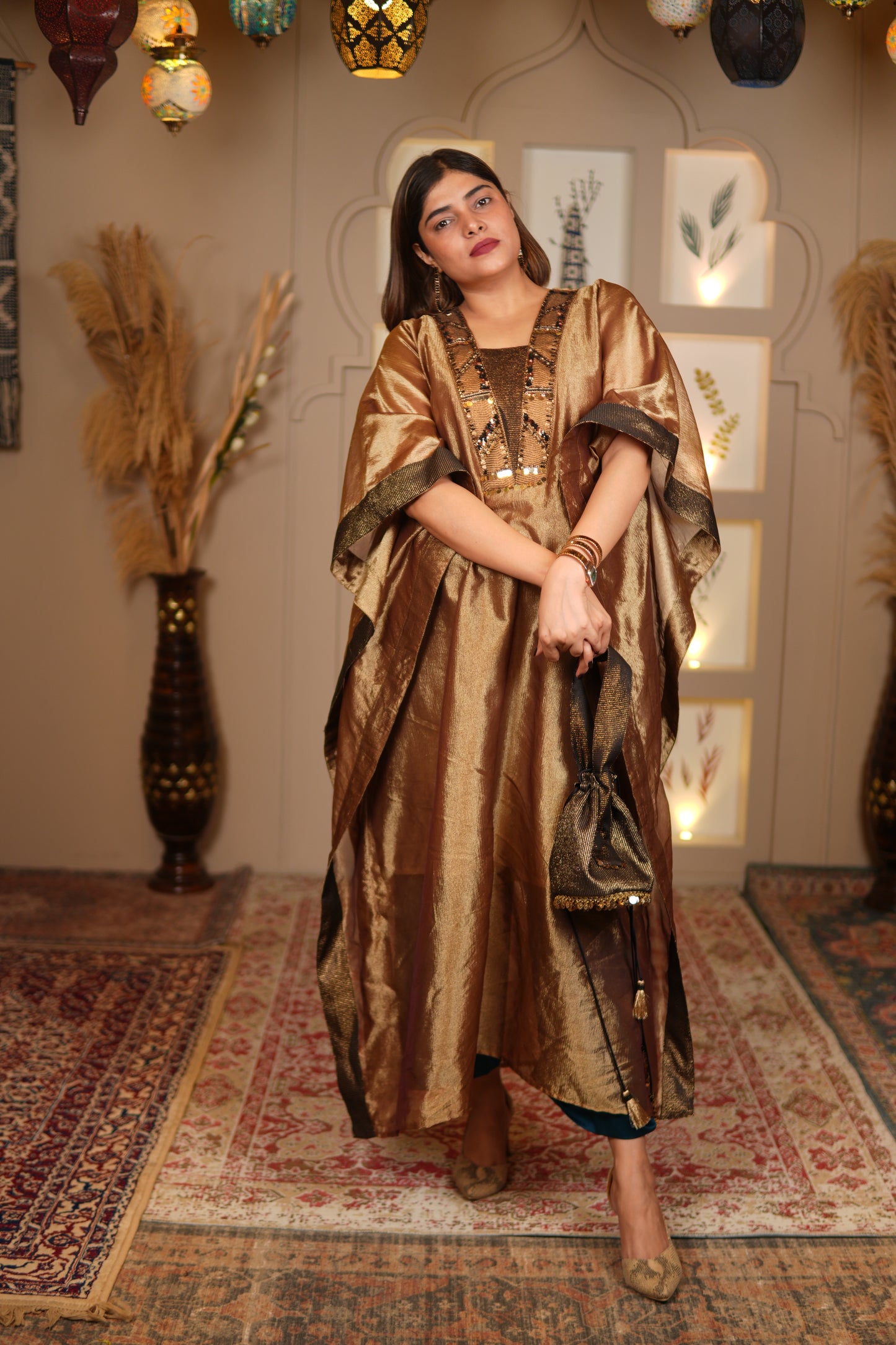 Woman in a gold dress standing in a room with patterned rug and decorative items.