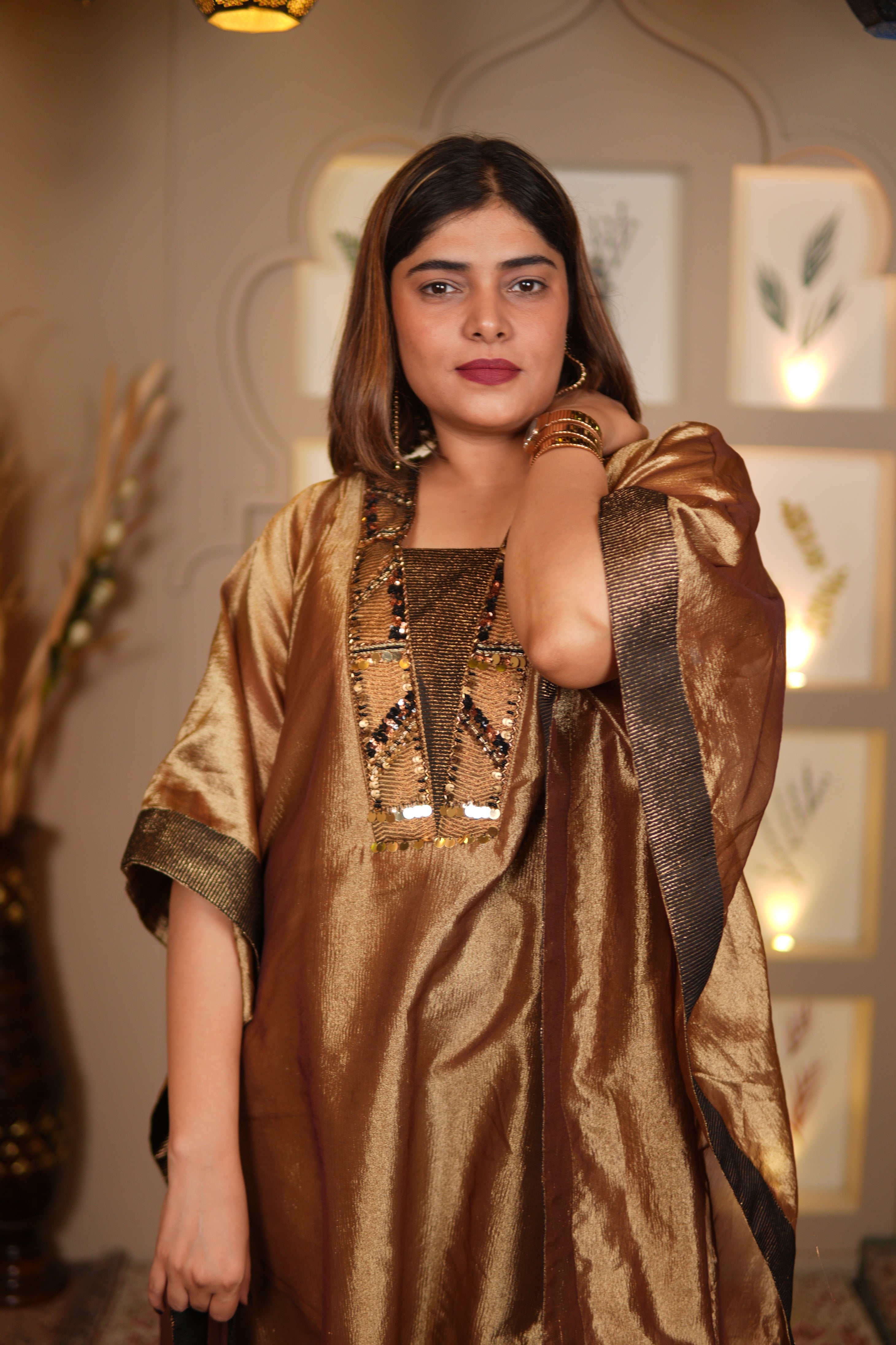 Woman wearing a gold and brown dress with intricate designs in an indoor setting.