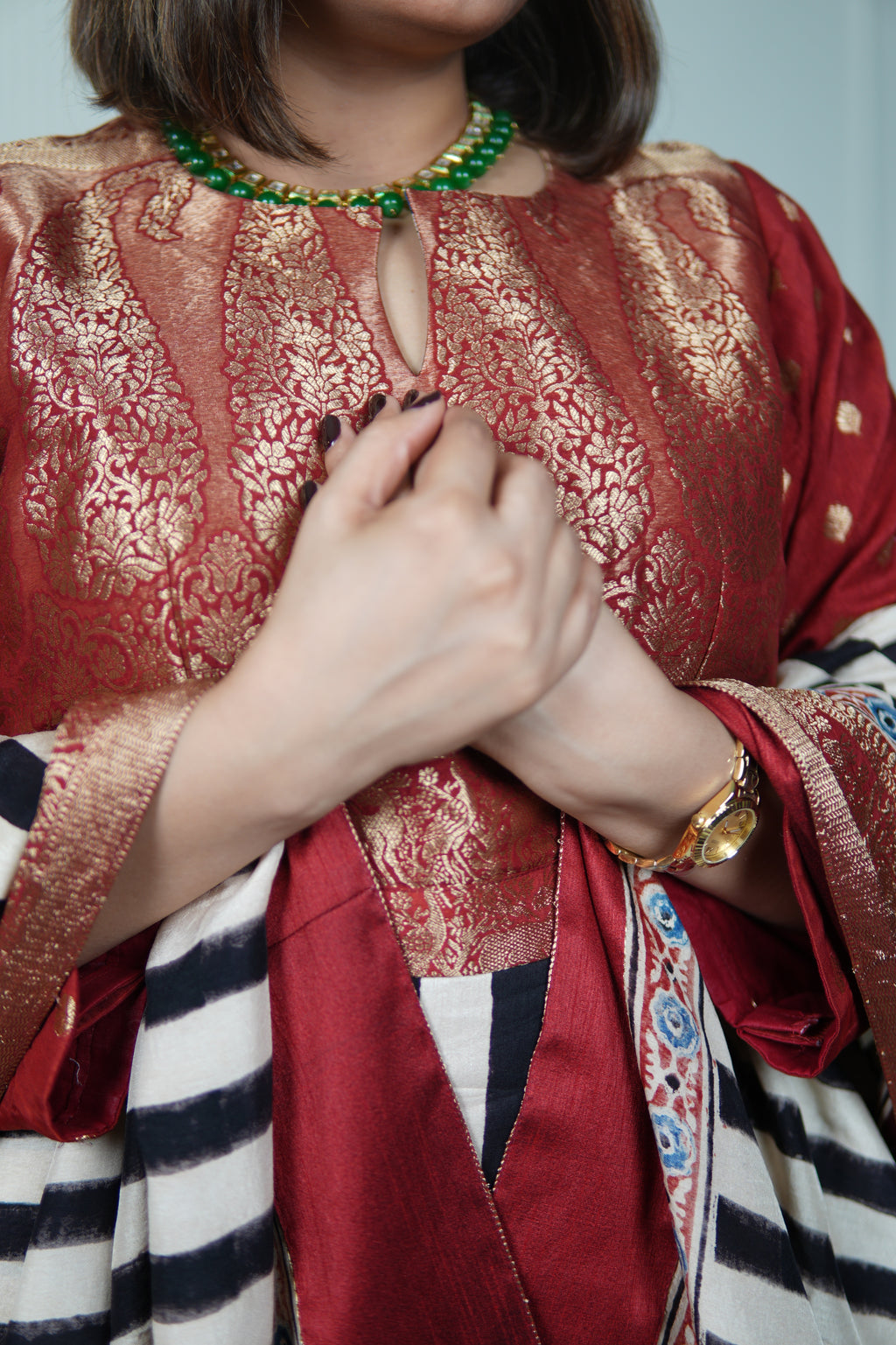 Person wearing a red traditional outfit with gold patterns, holding hands together.