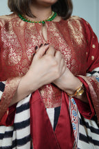 Person wearing a red traditional outfit with gold patterns, holding hands together.