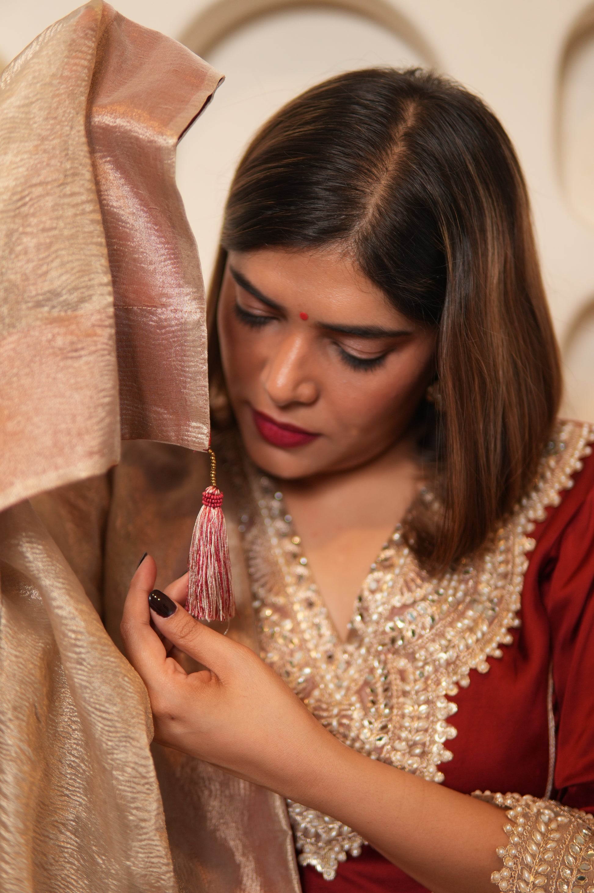 Woman in traditional attire highlighting a tassel on dupatta's edge.