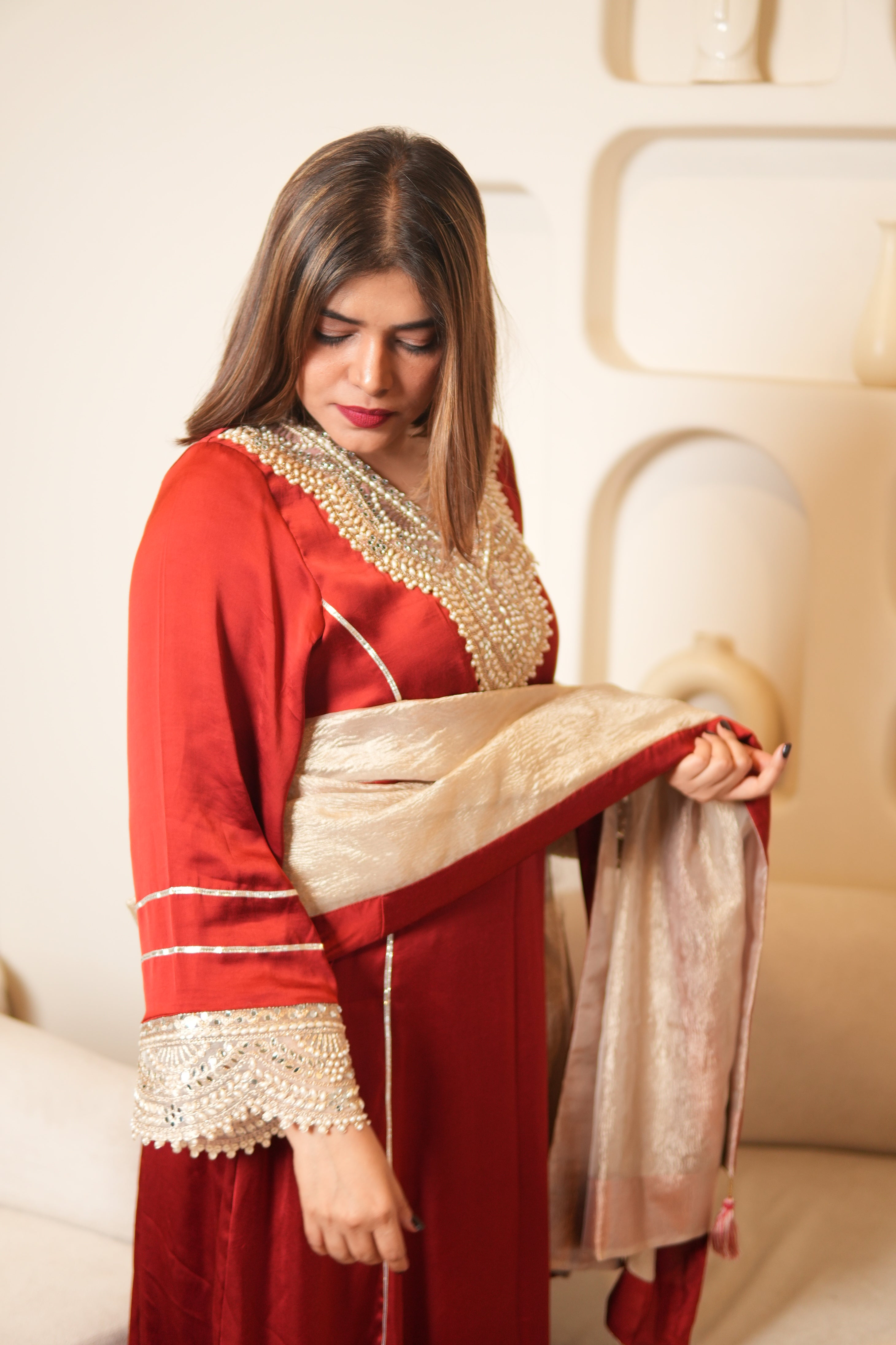 Woman wearing a red and gold traditional outfit on a beige sofa.