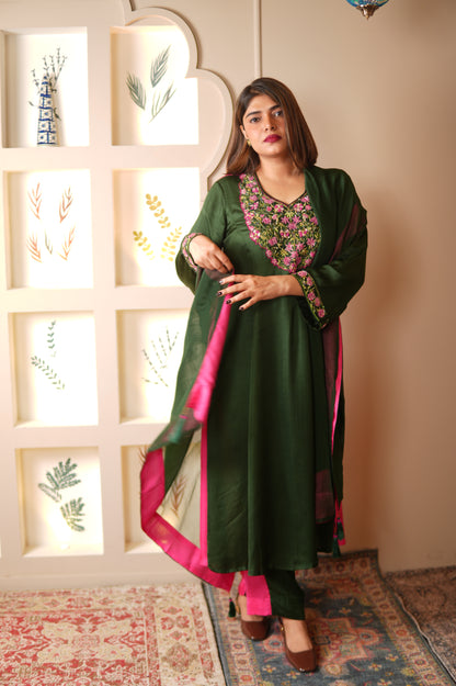 Woman in a green suit with green dupatta having pink border posing indoors.