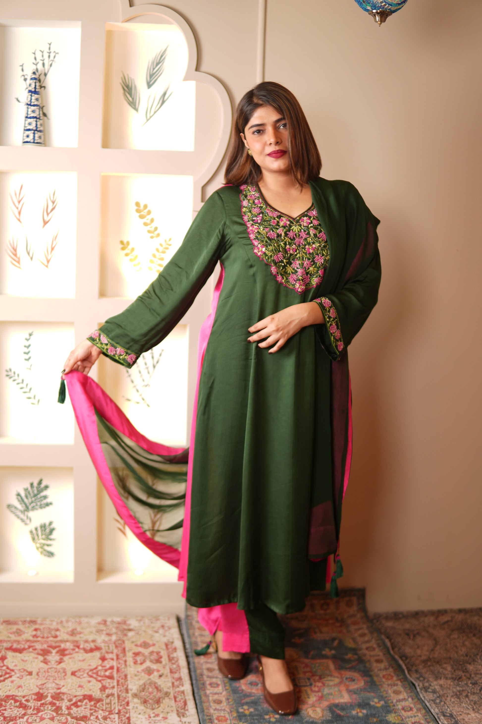Woman in a green traditional outfit with pink accents, standing indoors.