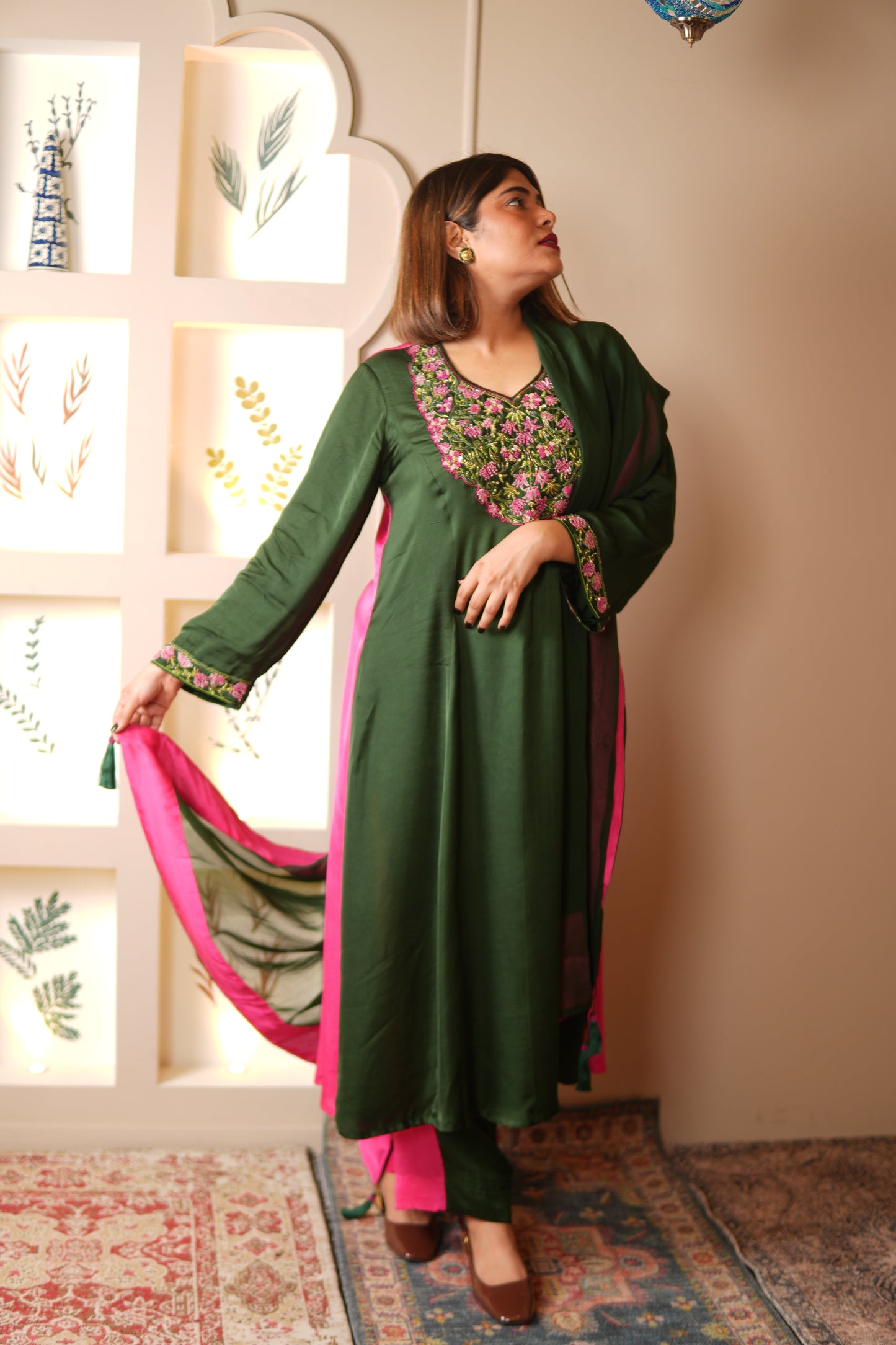 Woman wearing a green and pink traditional outfit in a room with patterned walls.