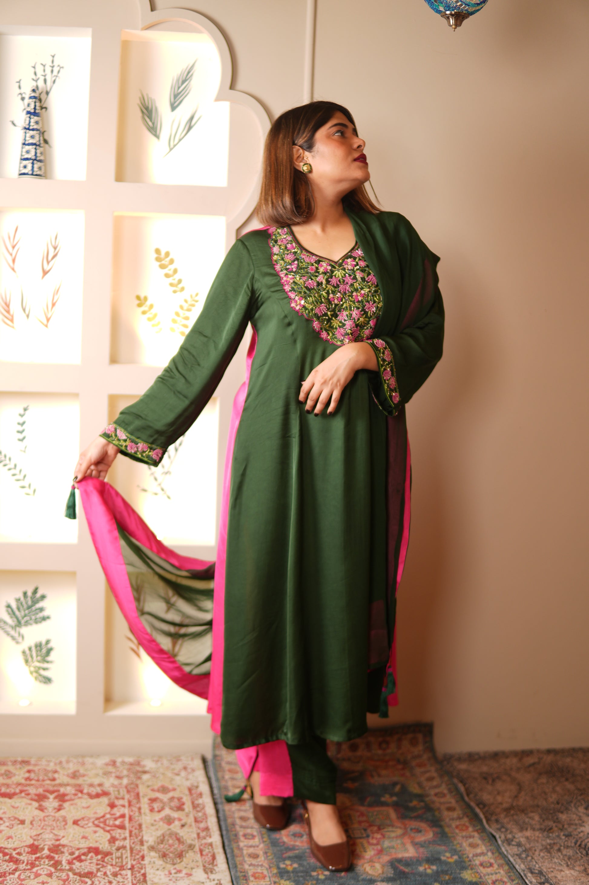 Woman wearing a green and pink traditional outfit in a room with patterned walls.