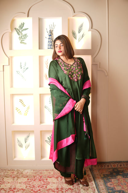 Woman in a green and pink traditional outfit lying on a decorative surface with a patterned wall in the background.