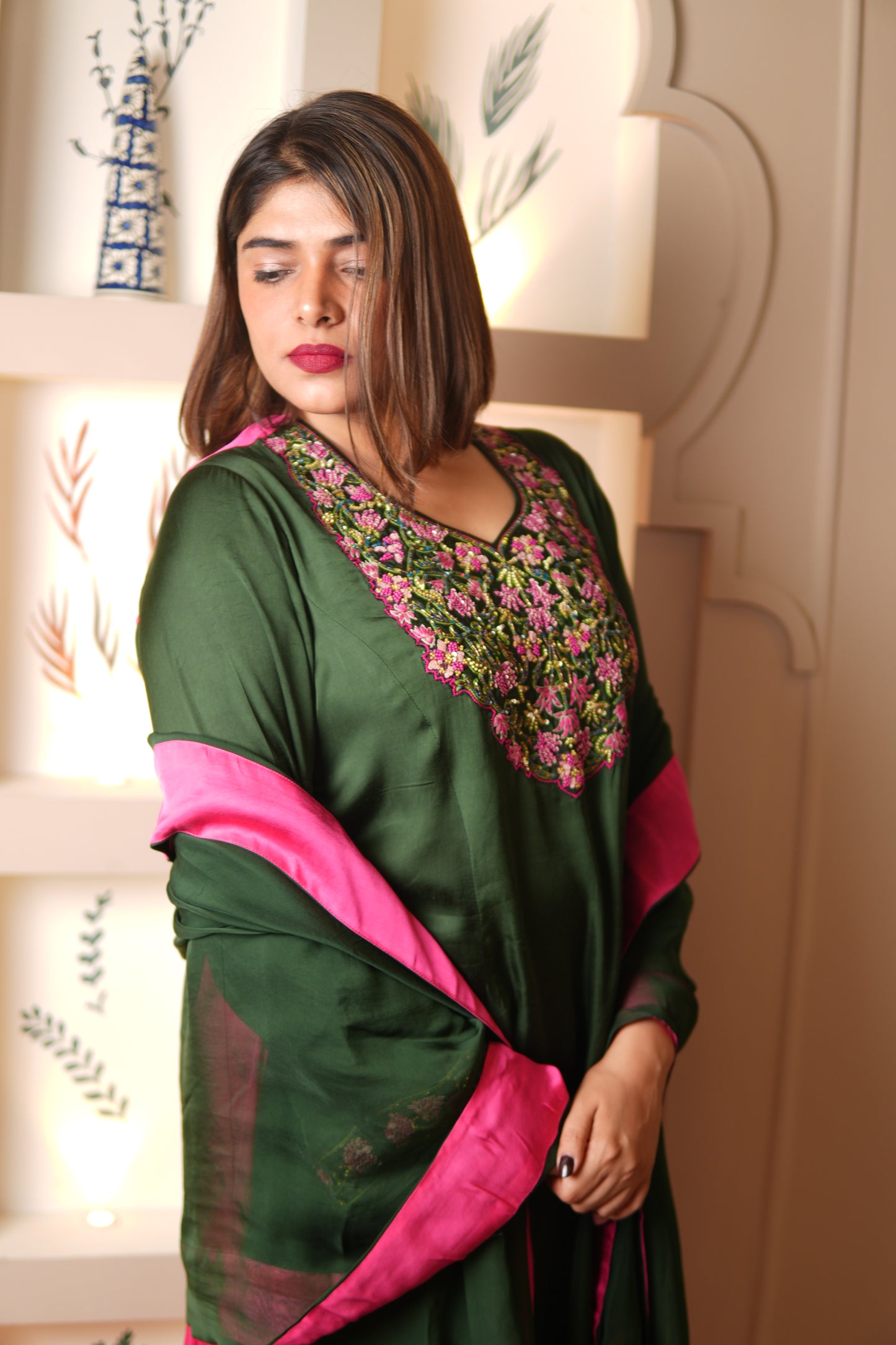 Woman wearing a green and pink traditional outfit with floral patterns indoors.