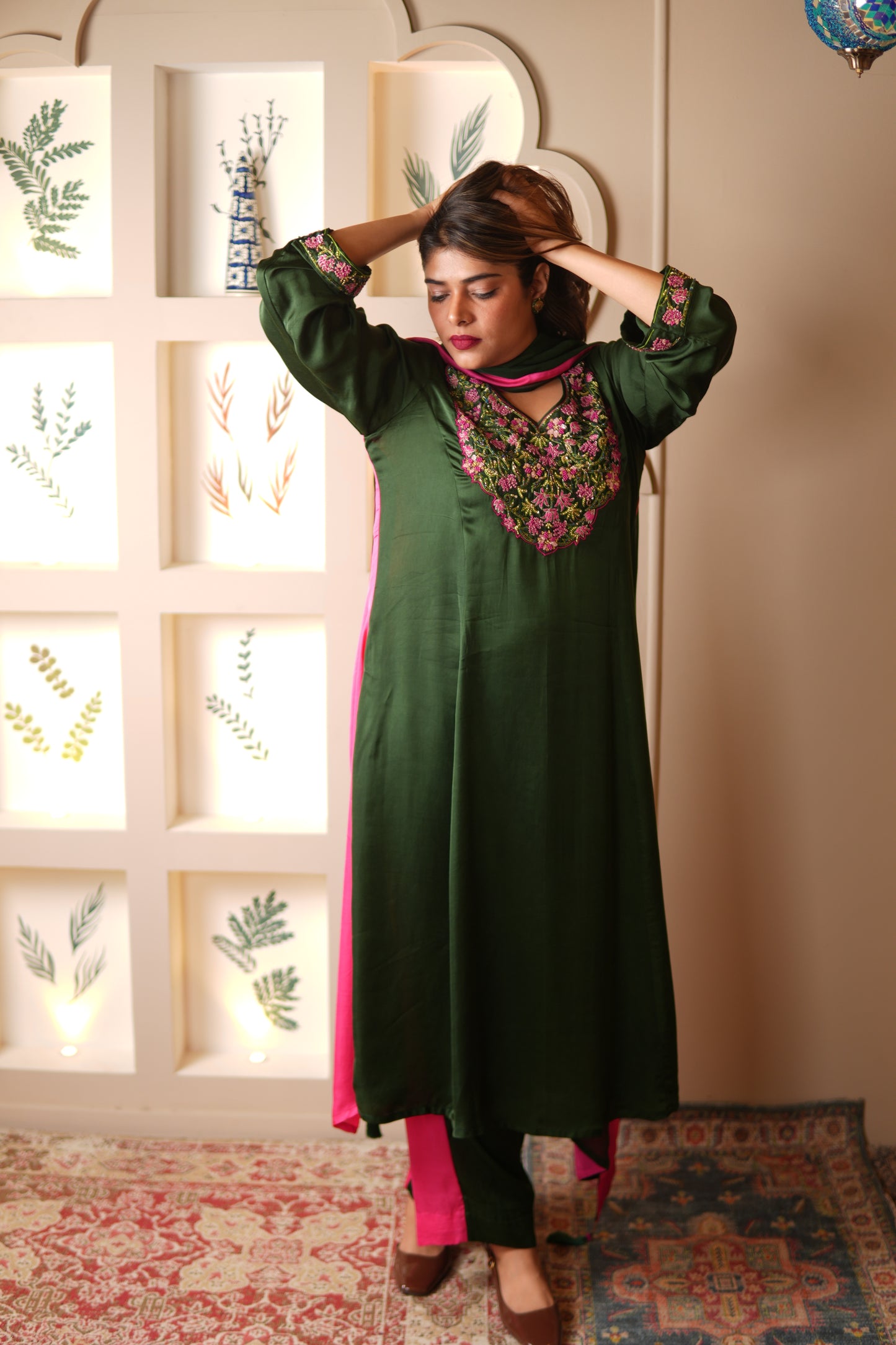 Woman in a green and pink suit with floral patterns standing in a room with decorative elements.