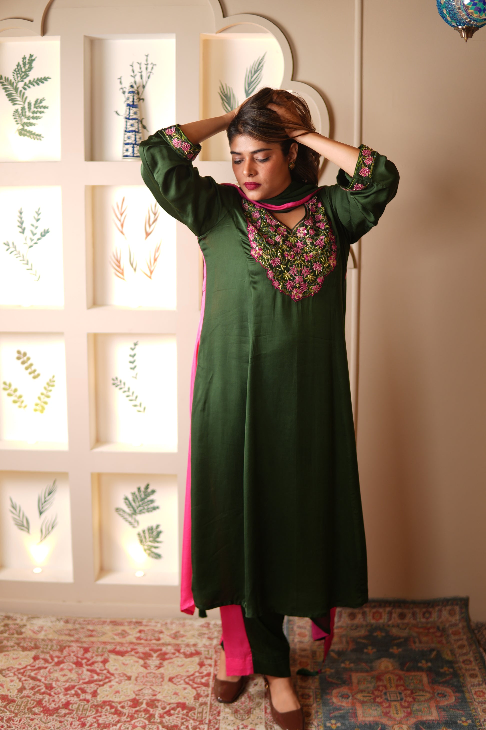 Woman in a green and pink suit with floral patterns standing in a room with decorative elements.