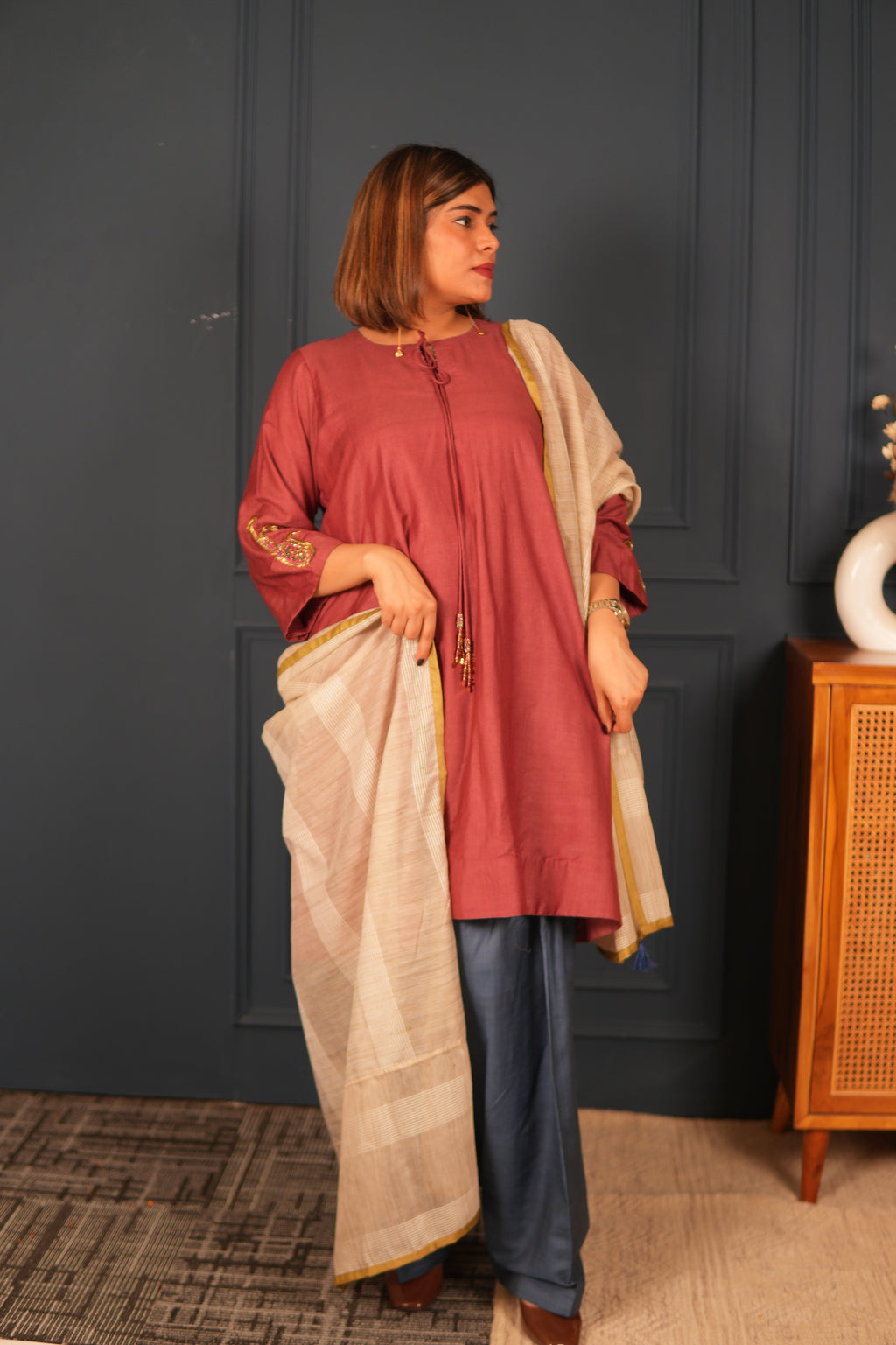 Person wearing a traditional outfit with a deep mauve Kurta and beige dupatta  against a dark wall.