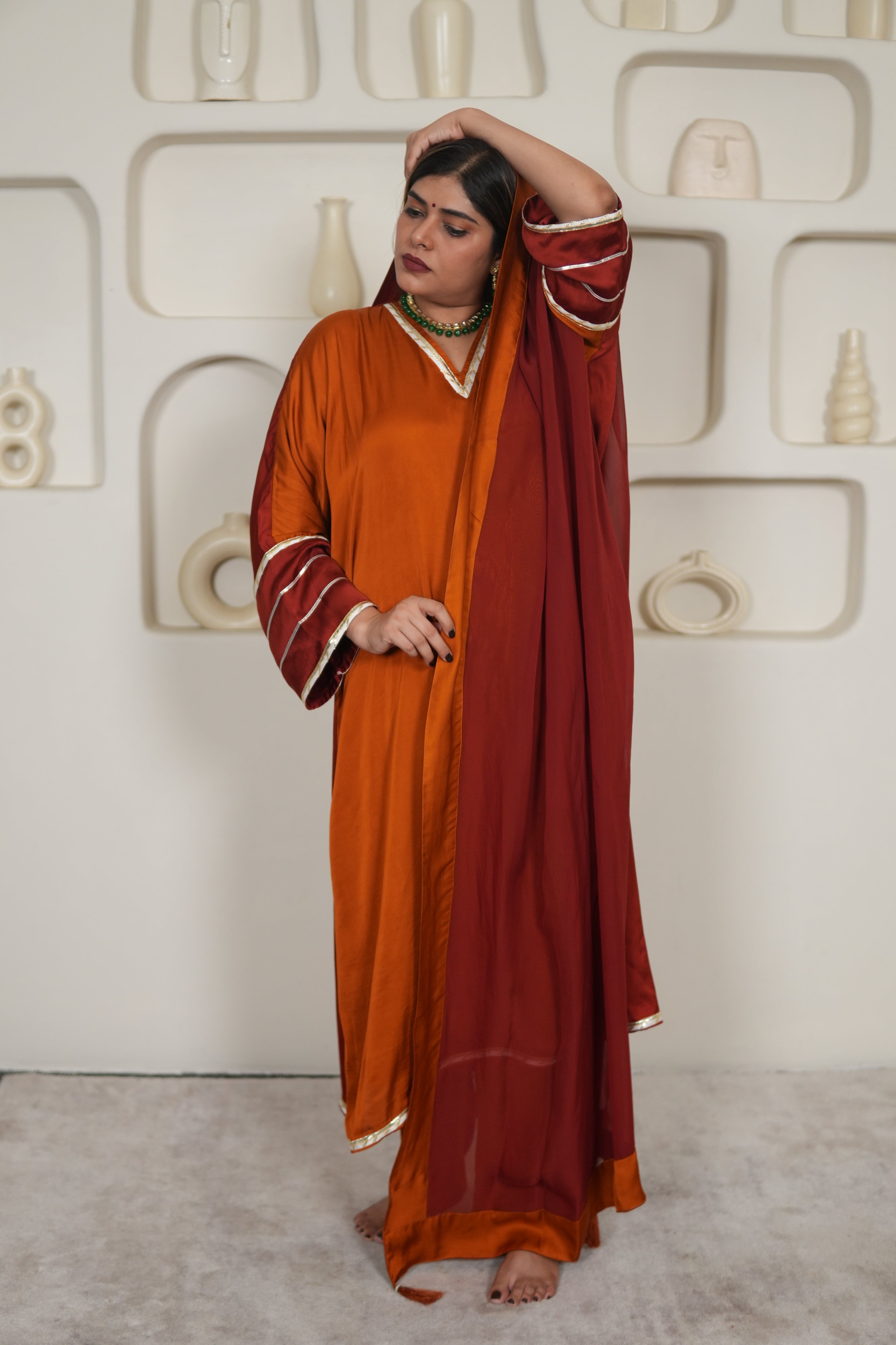 Person wearing a long, orange and red suit on a neutral background