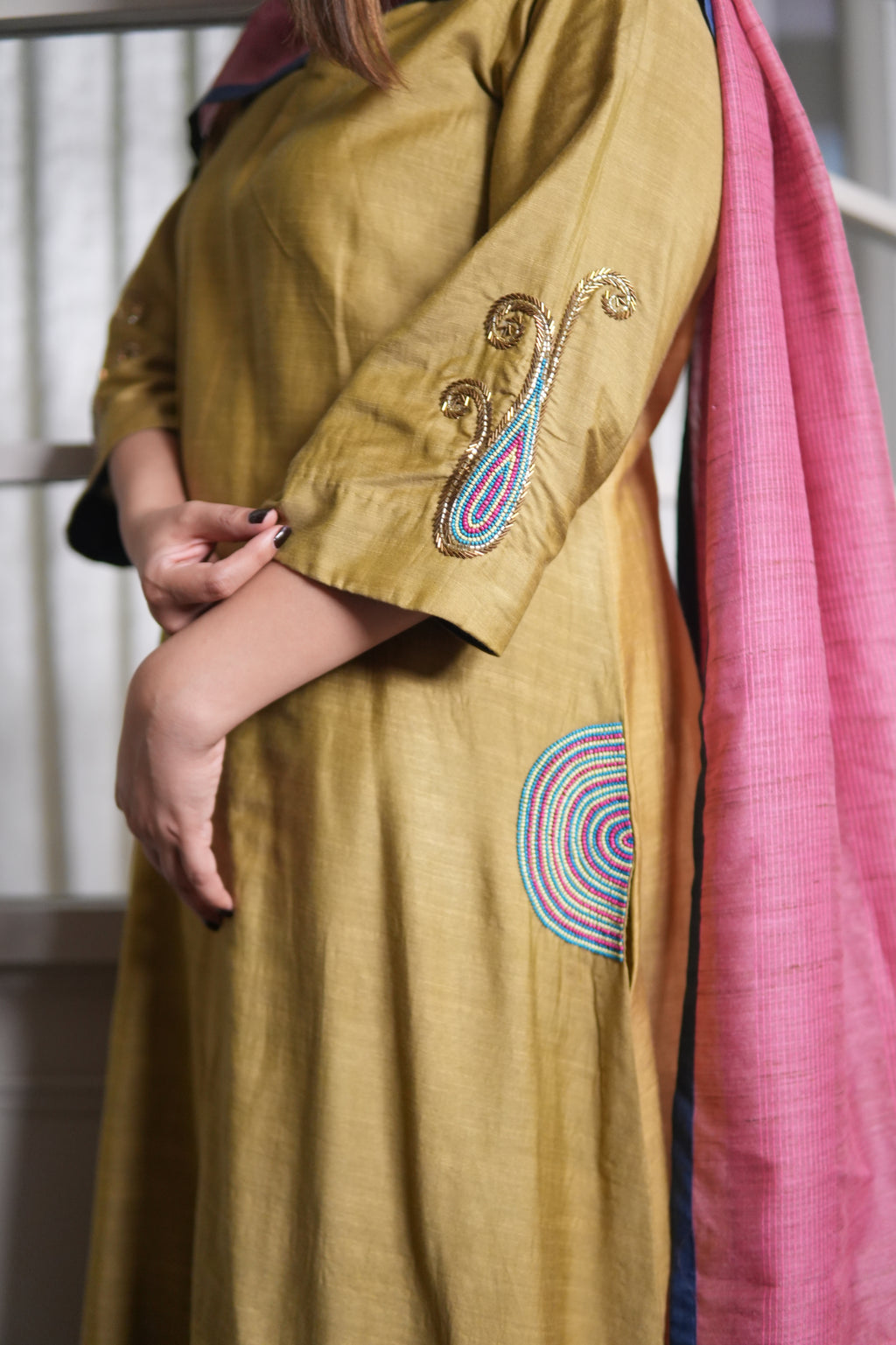 Close-up of a person wearing a mustard yellow saree with pink blouse, focusing on the fabric and design details.